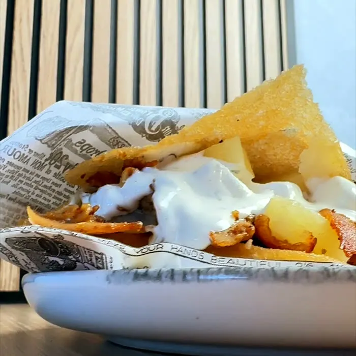 Papas de la casa con salsa y queso, sobre papel de periódico